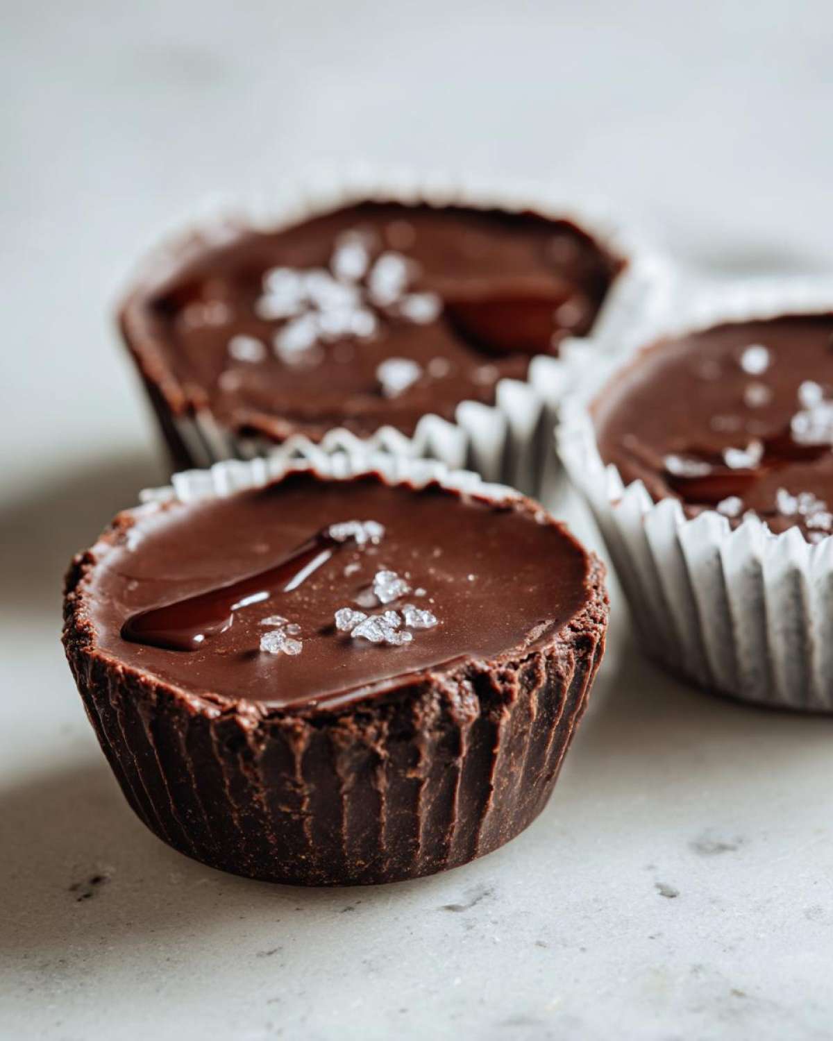 Three rich, dark chocolate Keto Chocolate Peanut Butter Fat Bombs topped with sea salt flakes.
