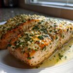 Two perfectly cooked fillets of Keto Garlic Butter Salmon glistening with melted butter and herbs on a white plate.