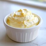 Close-up of fluffy, pale yellow Keto Lemon Cheesecake Mousse served in a small white fluted ramekin.