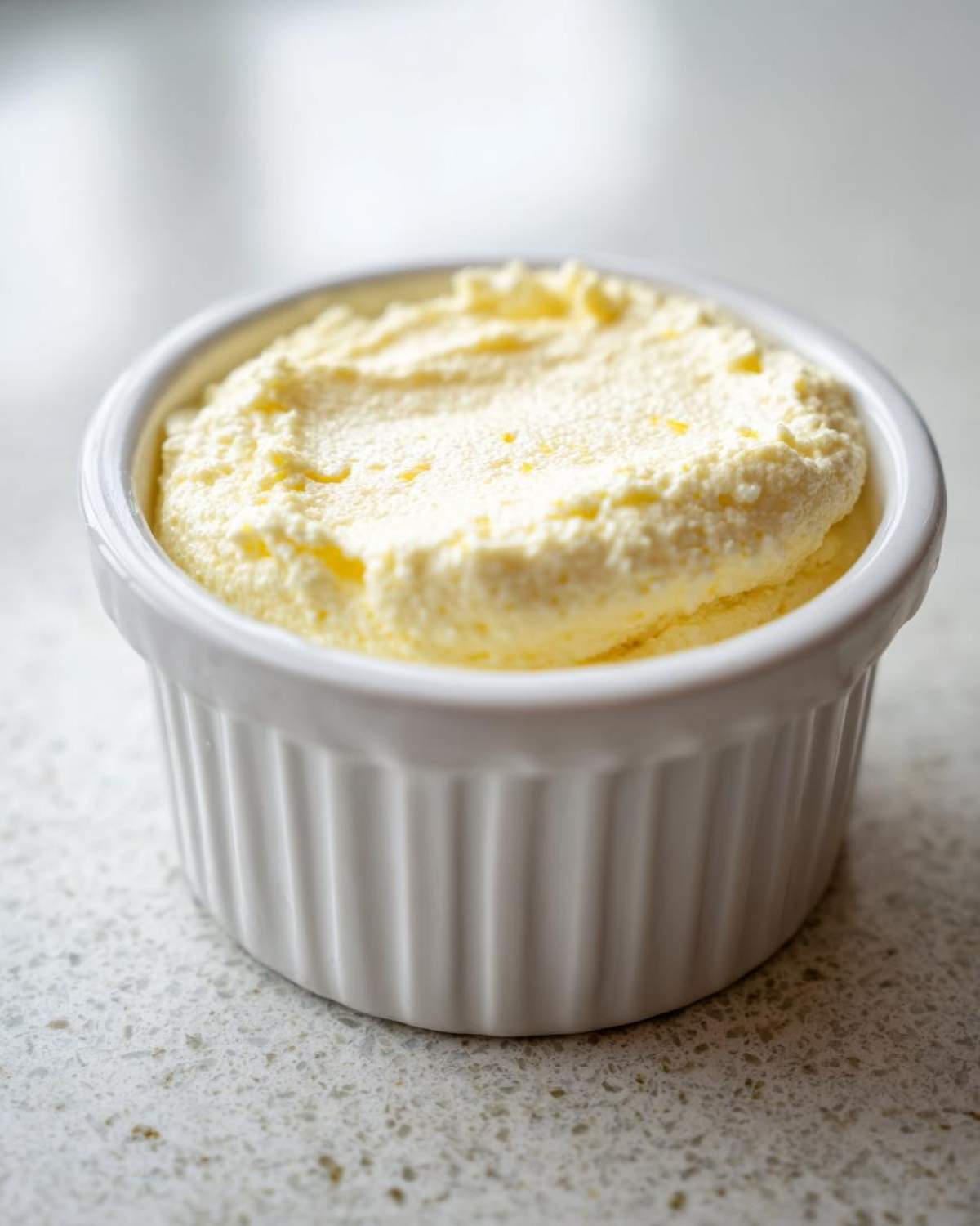 A single serving of light yellow Keto Lemon Cheesecake Mousse in a white fluted ramekin.