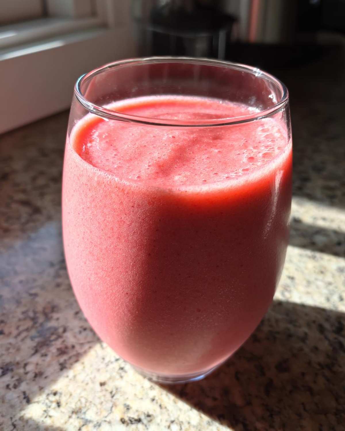 A close-up of a thick, pink Keto Strawberry Cheesecake Smoothie served in a clear glass on a granite countertop.