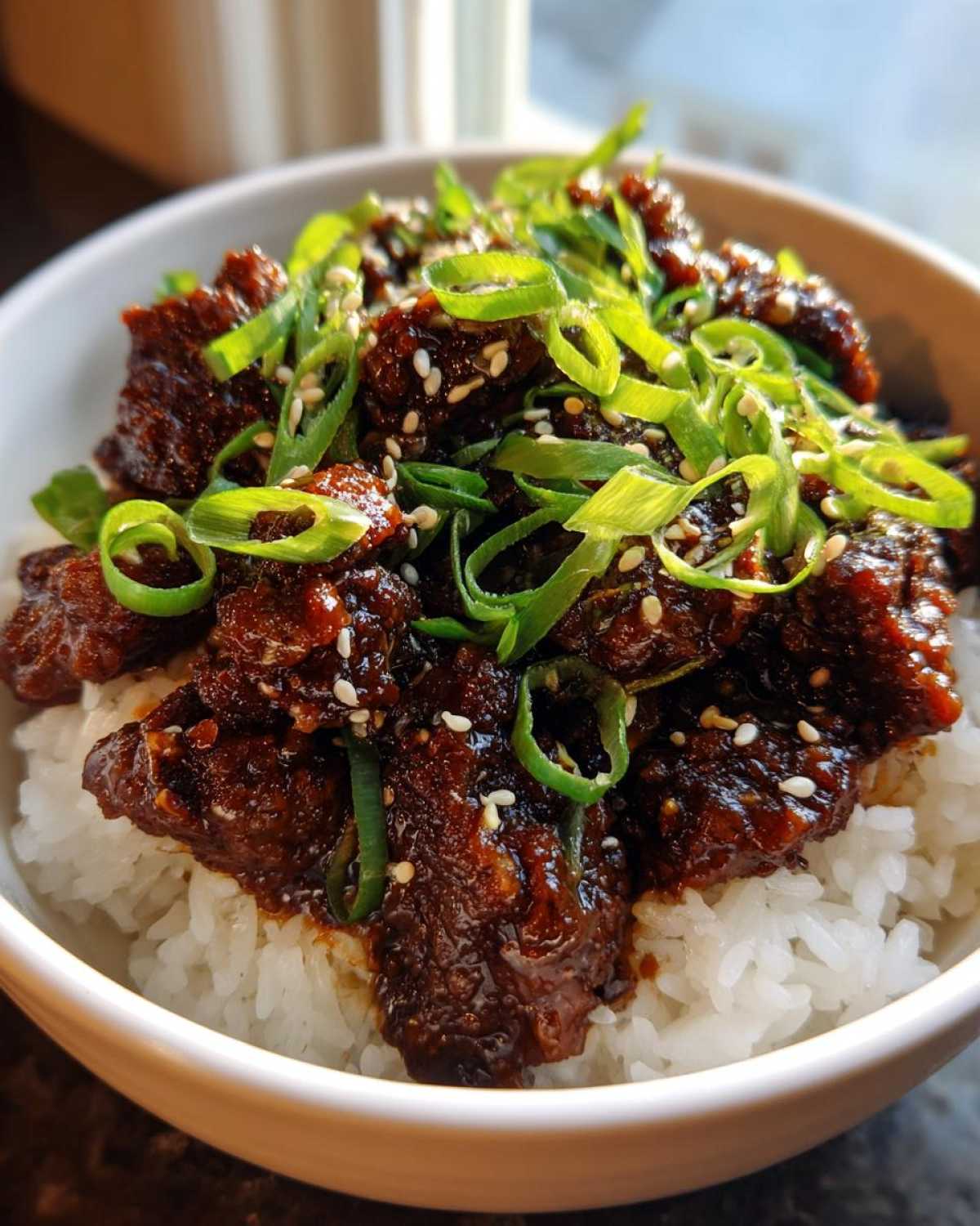 Close-up of a Korean Ground Beef Bulgogi Bowl with rich, dark sauce over white rice, garnished heavily with sliced green onions and sesame seeds.