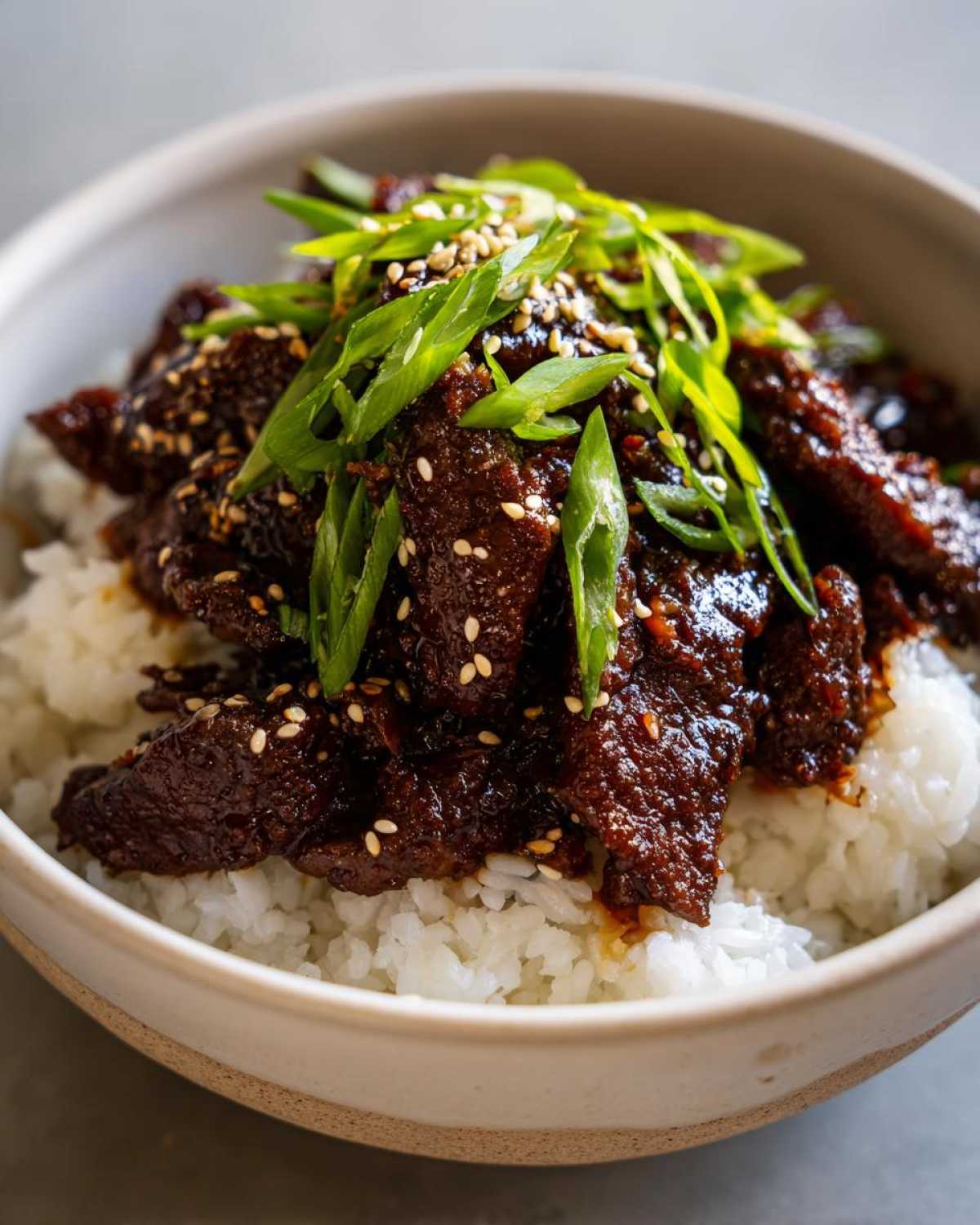 Close-up of Korean Ground Beef Bulgogi Bowls featuring rich, saucy beef over white rice, topped with green onions and sesame seeds.