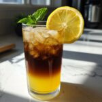 A tall glass featuring layered Cold Brew Lemonade with bright yellow lemonade on the bottom and dark cold brew coffee floating above ice.