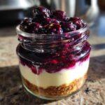 A single serving of Lemon Blueberry Cheesecake Jars showing graham cracker crust, creamy filling, and blueberry topping in a glass jar.