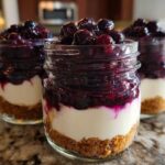 Three individual Lemon Blueberry Cheesecake Jars layered with graham cracker crust, creamy filling, and blueberry topping.