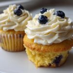 Two Lemon Blueberry Cupcakes with thick swirls of cream cheese frosting and fresh blueberries on top.