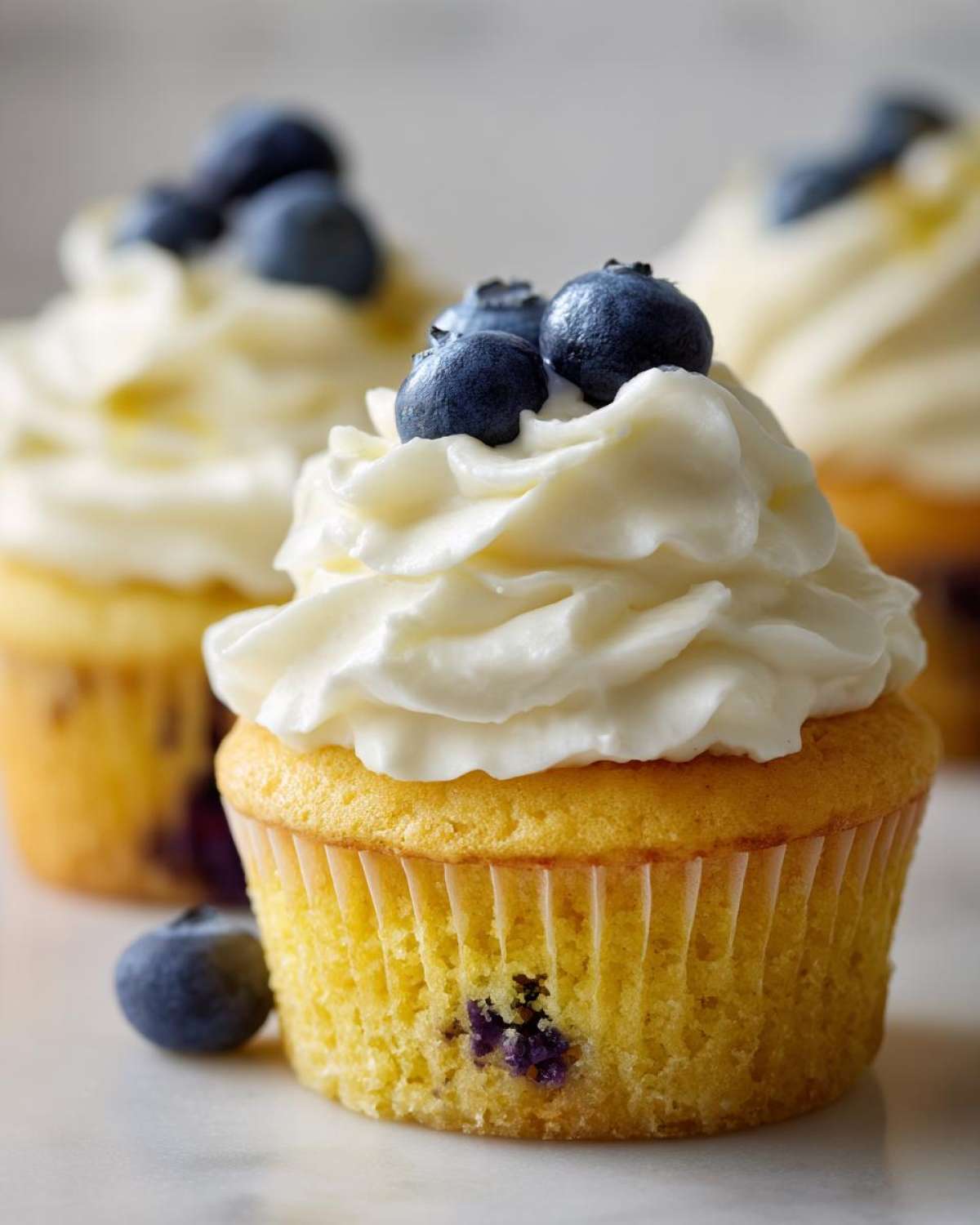 A close-up of a Lemon Blueberry Cupcake topped with swirls of cream cheese frosting and fresh blueberries.