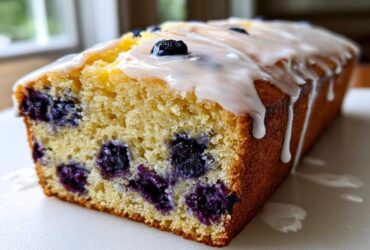 A close-up view of a freshly baked Lemon Blueberry Yogurt Loaf showing moist crumb and dripping lemon glaze.