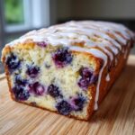 Close-up of a freshly baked Lemon Blueberry Yogurt Loaf, showing moist crumb packed with blueberries and drizzled with white glaze.