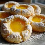 A plate of freshly baked Lemon Curd Thumbprint Cookies dusted generously with powdered sugar.