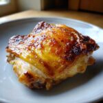 Close-up of a perfectly roasted Lemon Garlic Roasted Chicken Thighs with golden, crispy skin on a light plate.
