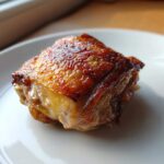 Close-up of a perfectly cooked piece of Lemon Garlic Roasted Chicken Thighs with glossy, crispy skin.