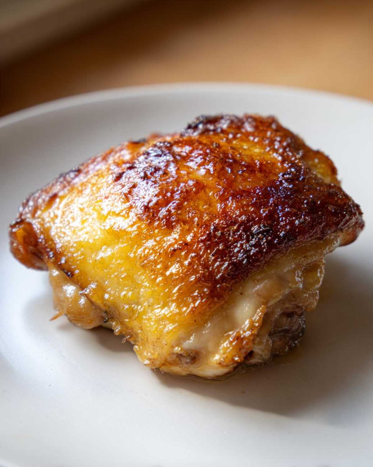 Close-up of a perfectly cooked Lemon Garlic Roasted Chicken Thighs with golden, crispy skin on a white plate.