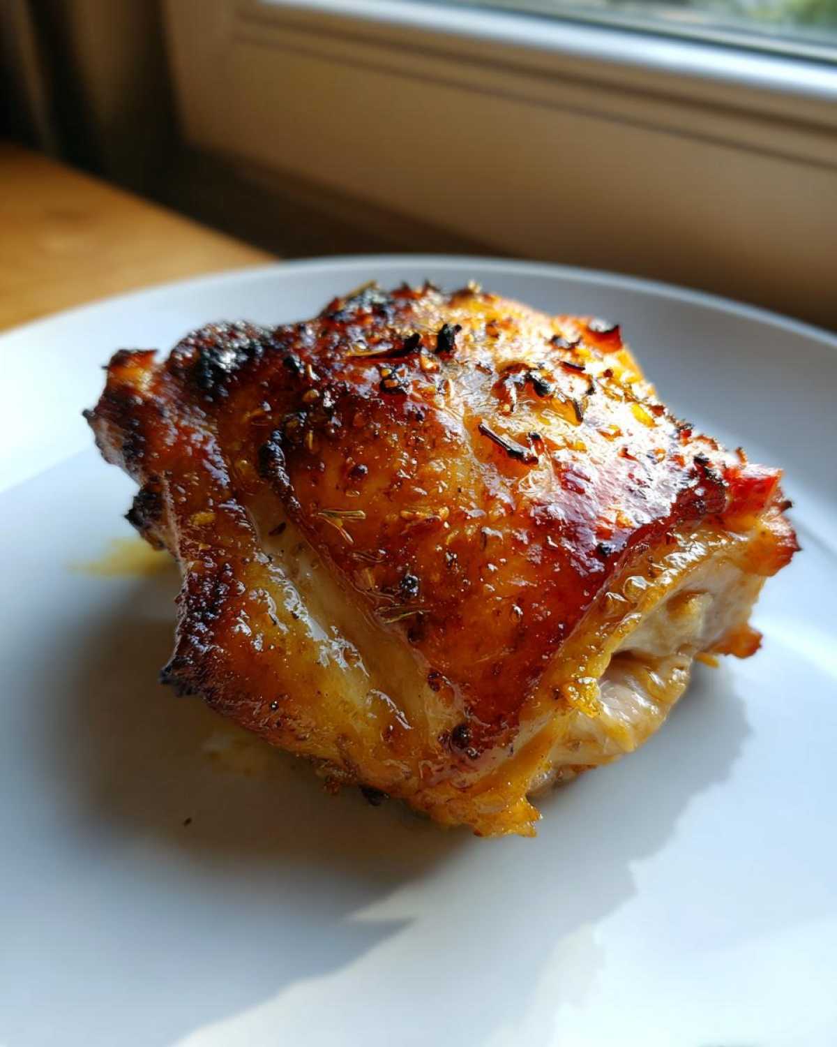 Close-up of a perfectly roasted, glistening Lemon Garlic Roasted Chicken Thighs with crispy skin and herbs.