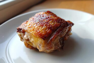 Close-up of a perfectly cooked piece of Lemon Garlic Roasted Chicken Thighs with glossy, crispy skin.