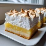 Close-up of a thick slice of Lemon Meringue Pie Bars showing crust, bright yellow filling, and peaks of toasted meringue.