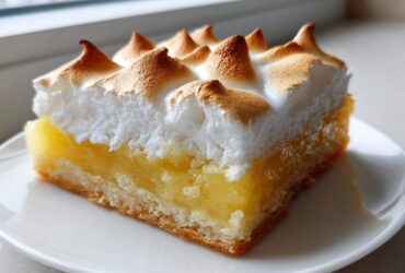 A close-up of a single serving of Lemon Meringue Pie Bars with a thick, toasted meringue topping.