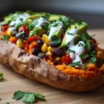 A close-up of a Loaded Veggie Stuffed Sweet Potato filled with black beans, corn, peppers, and topped with avocado slices and sour cream.