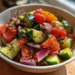 Close-up of a fresh Mediterranean Cucumber Tomato Salad with red onion, olives, and herbs in a white bowl.