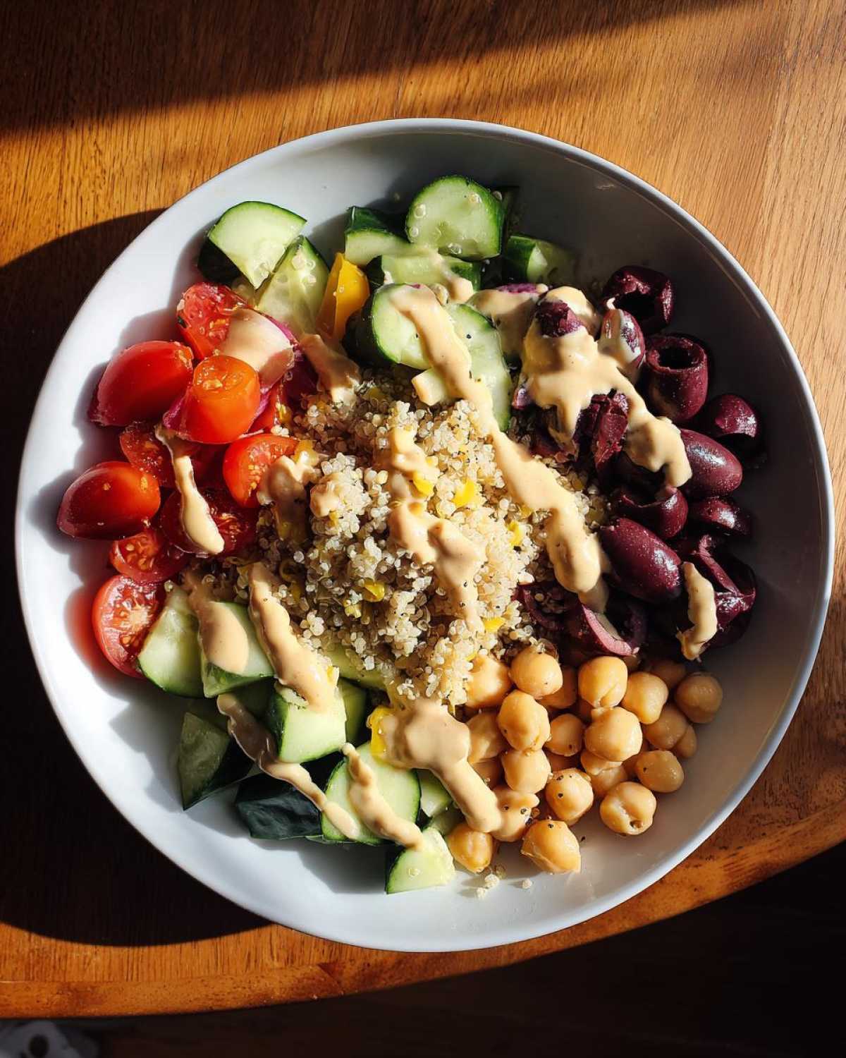 Overhead view of a Mediterranean Quinoa Bowl featuring quinoa, cucumbers, tomatoes, olives, chickpeas, and lemon tahini sauce.