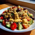 A vibrant Mediterranean Quinoa Bowl topped generously with creamy Lemon Tahini Sauce, chickpeas, tomatoes, and cucumbers.