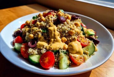 A vibrant Mediterranean Quinoa Bowl topped generously with creamy Lemon Tahini Sauce, chickpeas, tomatoes, and cucumbers.