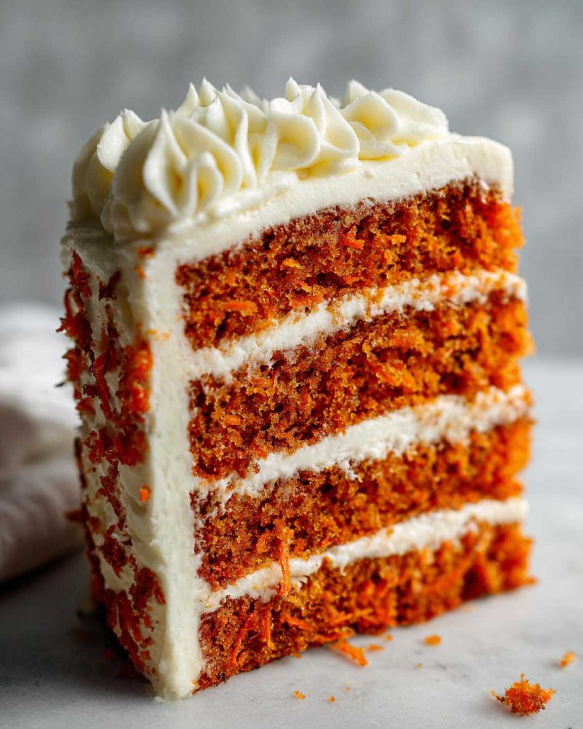 A tall, three-layer slice of Moist Carrot Cake with Cream Cheese Frosting, showing shredded carrots in the orange cake layers.