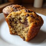 Close-up of a moist Chocolate Chip Banana Muffins cut open, revealing melted chocolate chunks inside.
