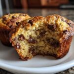 Close-up of a moist Chocolate Chip Banana Muffins, broken open to show texture and chocolate chips inside.