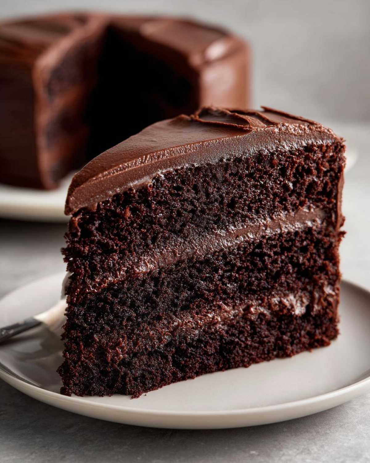Close-up of a rich, moist slice of Gluten-Free Chocolate Cake with thick chocolate frosting layers.