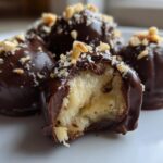 Close-up of No-Bake Chocolate Covered Banana Bites, one bitten open revealing the banana center, topped with chopped nuts.
