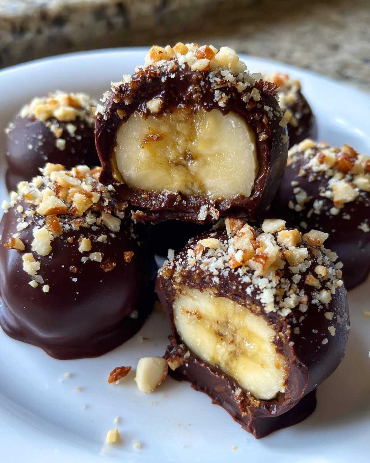 Close-up of No-Bake Chocolate Covered Banana Bites, showing a banana center dipped in dark chocolate and topped with chopped nuts.