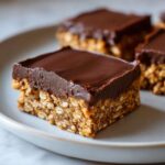 A close-up of a square No-Bake Chocolate Peanut Butter Oat Bar with a thick chocolate topping on a light gray plate.