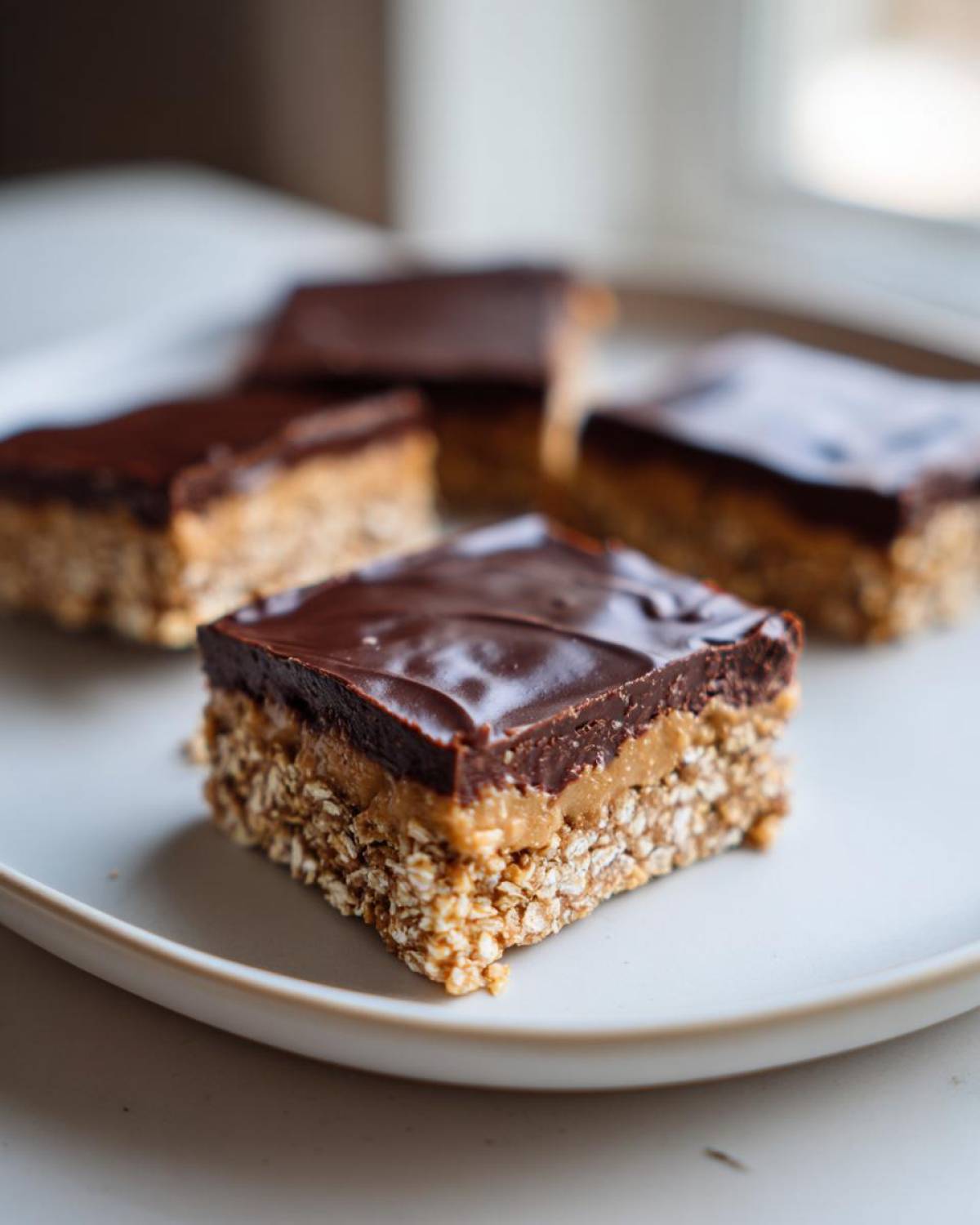 A close-up of one square of No-Bake Chocolate Peanut Butter Oat Bars showing the oat base, peanut butter layer, and chocolate topping.