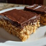 Two squares of No-Bake Chocolate Peanut Butter Oat Bars with a thick chocolate topping resting on a white plate.