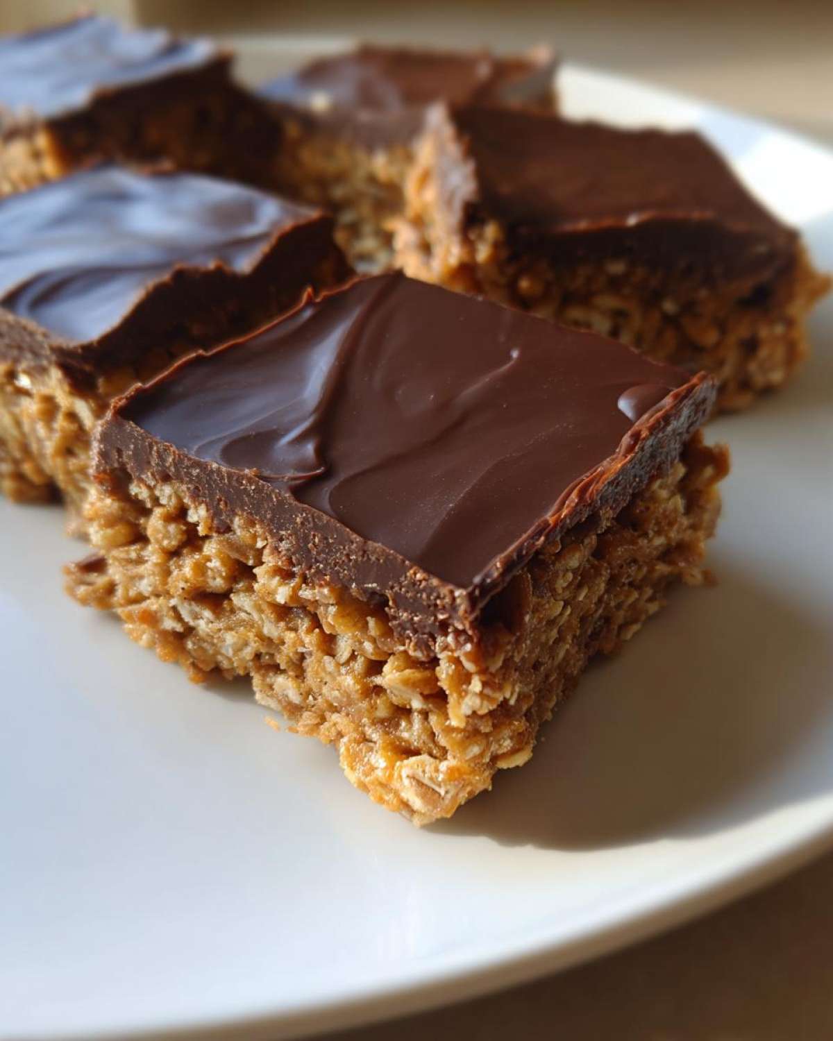 A square portion of No-Bake Chocolate Peanut Butter Oat Bars with a thick chocolate topping on a white plate.