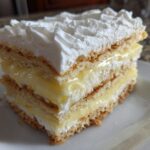 A layered slice of No-Bake Lemon Icebox Cake featuring graham cracker layers, lemon filling, and piped whipped cream.
