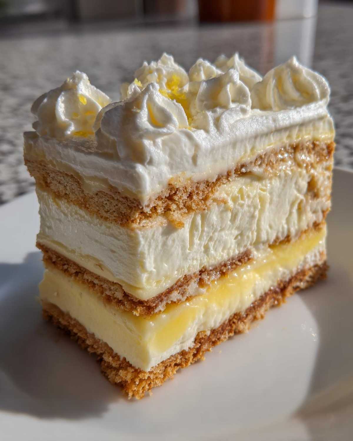 Close-up of a layered slice of No-Bake Lemon Icebox Cake showing graham cracker layers, lemon filling, and whipped cream.