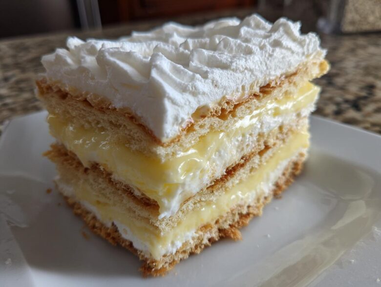 A layered slice of No-Bake Lemon Icebox Cake featuring graham cracker layers, lemon filling, and piped whipped cream.