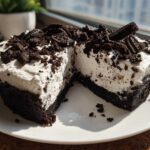 A close-up of a slice of No-Bake Oreo Cheesecake showing the dark crust and creamy filling topped with cookie crumbles.