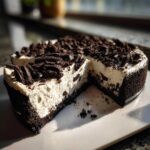 A rich slice cut from a No-Bake Oreo Cheesecake, showing the creamy white filling and dark cookie crust, topped with crushed Oreos.