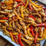 Close-up of seasoned chicken strips mixed with roasted red, yellow, and orange peppers and onions for One-Pan Chicken Fajitas.