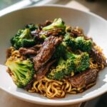 Close-up of tender beef strips and bright green broccoli florets mixed with ramen noodles in a savory sauce.