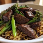 Close-up of tender beef chunks and bright green broccoli mixed with ramen noodles in a savory sauce.
