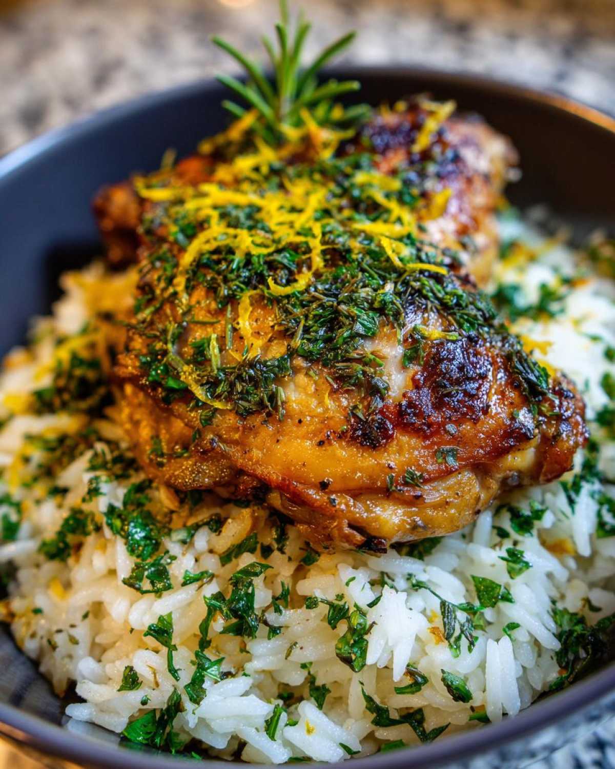 Close-up of crispy chicken thigh served over fluffy rice, topped with lemon zest and fresh herbs for One-Pot Chicken and Rice with Lemon and Herbs.