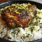 Close-up of One-Pot Chicken and Rice with Lemon and Herbs, featuring crispy chicken over white rice with lemon zest and parsley.