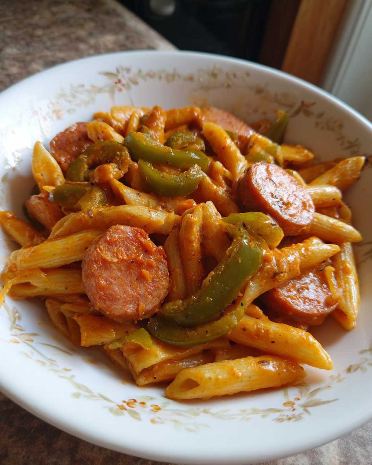 A close-up of a bowl filled with One-Pot Creamy Cajun Sausage Pasta, featuring penne, sliced sausage, and green bell peppers.