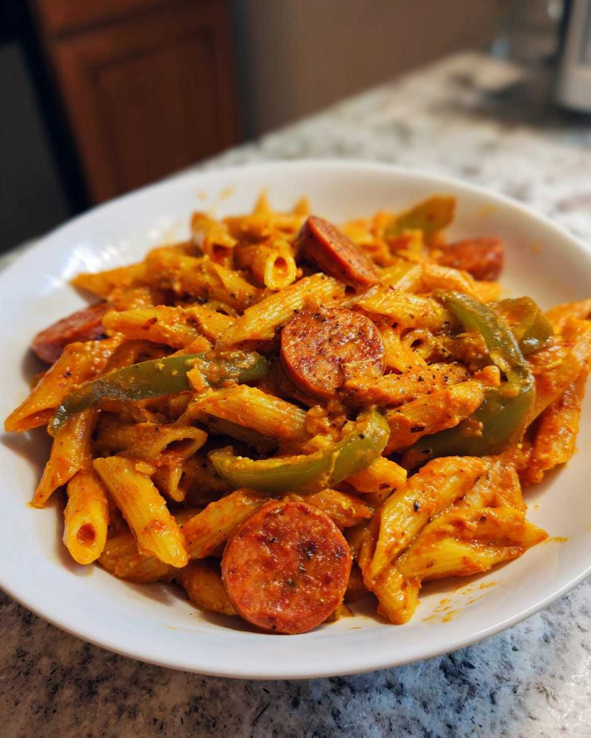 A close-up of One-Pot Creamy Cajun Sausage Pasta featuring penne, sliced sausage, and green bell peppers in a white bowl.