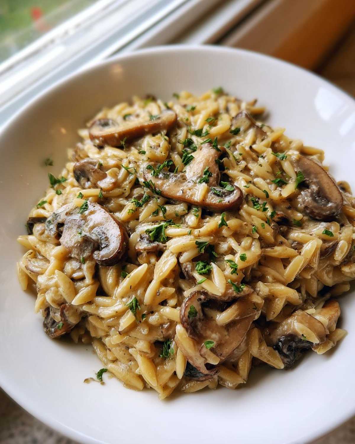 A close-up of a white bowl filled with creamy One-Pot Creamy Mushroom Orzo, topped with sliced mushrooms and parsley.